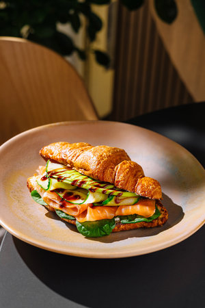 Freshly baked croissant with tasty filling of salmon, cucumber slices and sauce served on plate in cafeの写真素材