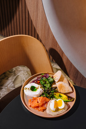 Delicious and healthy breakfast plate combining smoked salmon, poached egg and avocado on a wooden tableの写真素材