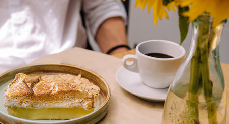 Lemon meringue pie and cup of coffee sit on a cafe table with a customer sitting in front, enjoying the food and atmosphereの写真素材