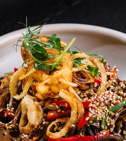 Gourmet spicy noodles with vegetables and seeds served in a white bowl on a dark textureの写真素材