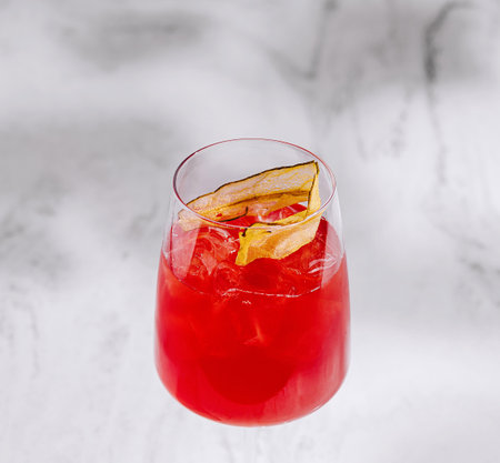 Elegant glass of vibrant red cocktail adorned with a twist of citrus on iceの写真素材