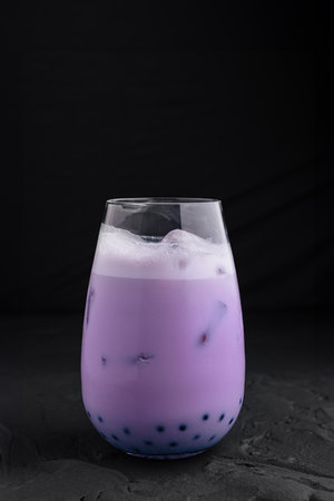 Glass of taro root tea with milk and tapioca pearls standing on a black backgroundの写真素材