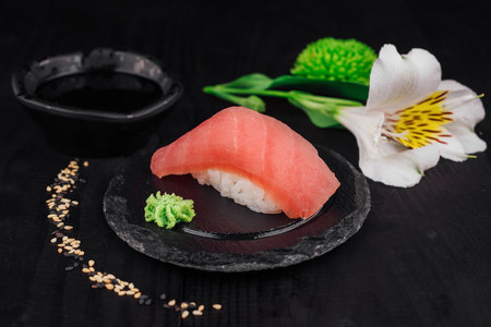 Freshly made maguro nigiri sushi served on a black slate with wasabi, soy sauce and flowersの写真素材