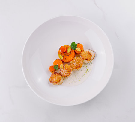 Delicious scallops cooked to perfection and served with a carrot garnish on a white plateの写真素材