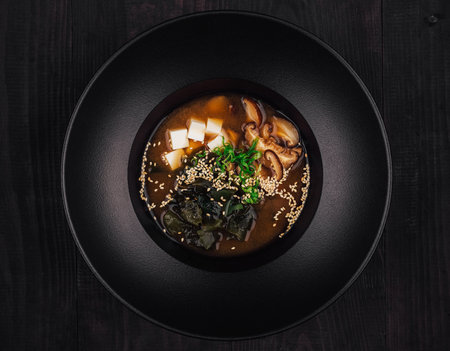 Steaming bowl of miso soup is served in a black bowl, garnished with chopped green onions and sesame seedsの写真素材