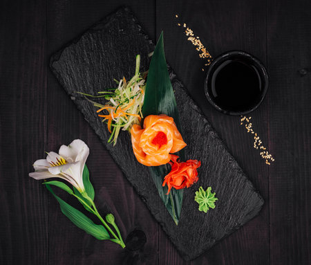 Delicious salmon sashimi appetizer served on black slate with wasabi, pickled ginger, soy sauce and white flowerの写真素材