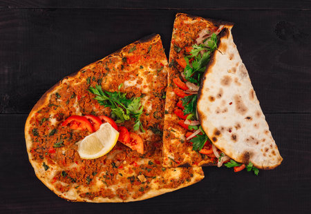 Turkish flatbread lahmacun with minced meat, tomatoes, parsley, spices served with lemon on dark...