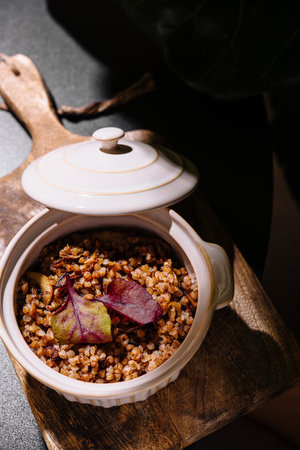 Buckwheat porridge with mushrooms and beetroot leaves served in a ceramic pot on a wooden board, creating a rustic and appetizing culinary sceneの写真素材