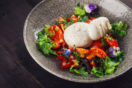 Fresh burrata cheese served on a bed of lettuce and tomatoes with a light vinaigrette dressingの写真素材
