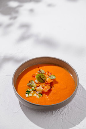 Bowl is filled with vibrant, creamy tomato soup and topped with fresh shrimp, cucumber, and greensの写真素材