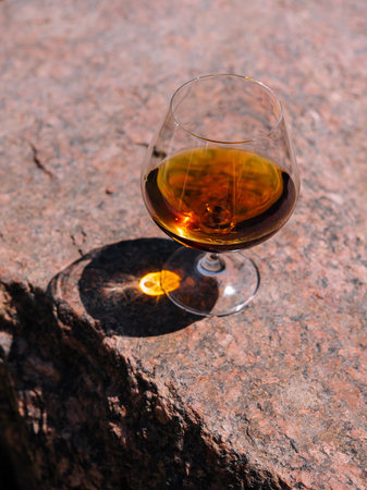 Glass of cognac is casting a long shadow on a rock on a bright sunny dayの写真素材