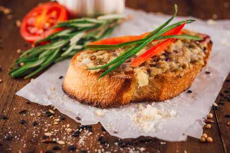 Toasted slice of baguette topped with spread and fresh herbs is presented on a wooden tableの写真素材
