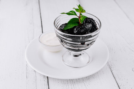 Glass bowl filled with prunes and garnished with fresh mint leaves, served on a white wooden tableの写真素材