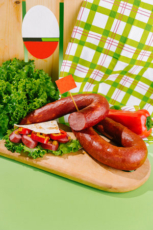 Smoked sausage with herbs and spices is lying on a wooden cutting board on a green backgroundの写真素材