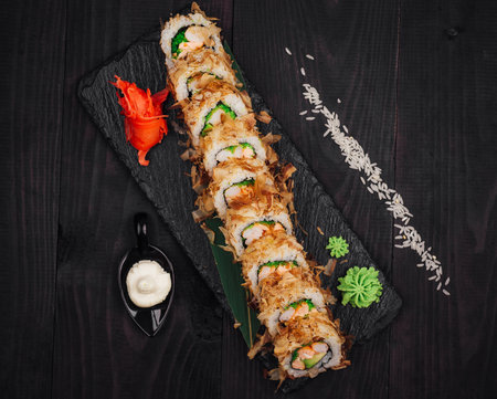 Delicious tempura sushi roll with fish and avocado being served on black slate platter with ginger, wasabi and scattered riceの写真素材
