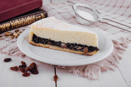 Delicious slice of poppy seed cake with cottage cheese filling sprinkled with powdered sugar sitting on white plateの写真素材