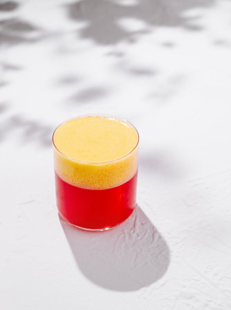 Refreshing two colored layered cocktail with yellow and red parts is standing on white table with shadowsの写真素材