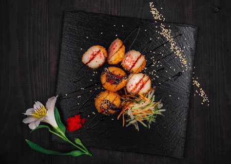 Delicious fried sushi balls being served on a black stone plate decorated with sauce, sesame seeds and a flowerの写真素材