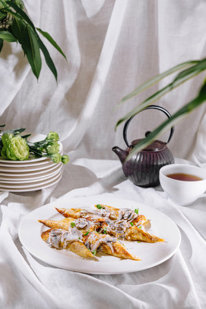 Four savory stuffed crepes are laying on a white plate, covered with creamy sauce and decorated with green onionsの写真素材