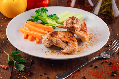 Delicious roasted chicken wings served with celery and carrot sticks on white plate on wooden table, perfect lunch ideaの写真素材