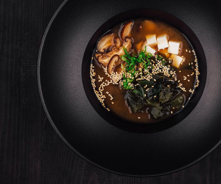 Aromatic miso soup with tofu, shiitake mushrooms, wakame seaweed and sesame seeds is served in a black bowlの写真素材