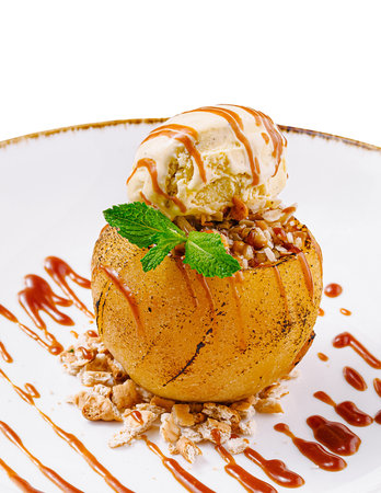 Delicious baked apple dessert with ice cream, caramel sauce and nuts, served on white plateの写真素材