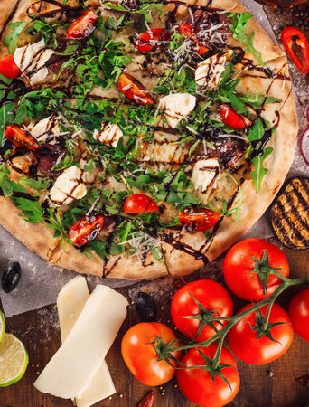 Delicious pizza with mozzarella, tomatoes and arugula decorated with balsamic glaze surrounded by fresh ingredientsの写真素材