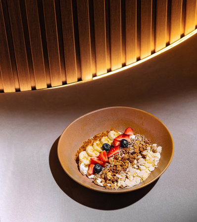 Plate of granola with yogurt, strawberries, blueberries and banana slices is served on a tableの写真素材