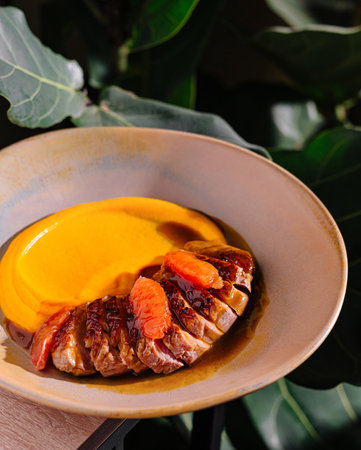 Duck breast with orange sauce and mashed sweet potatoes being served on a plate in a restaurantの写真素材