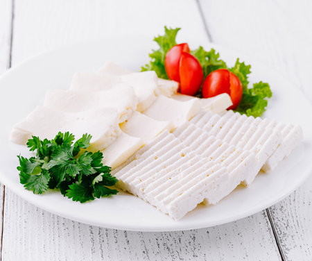 White plate with sliced white cheese, cherry tomatoes, and parsley is sitting on a white wooden tableの写真素材