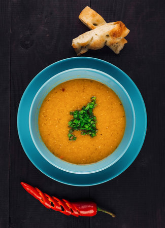 Delicious soup served in a bowl with chives, chili pepper and bread on the side, shot from above on a dark wooden backgroundの写真素材