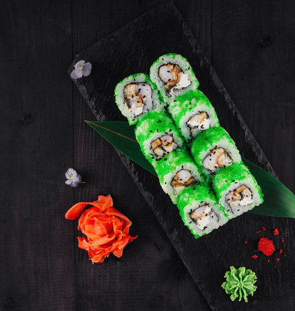 Green dragon sushi rolls decorated with flowers on a black wooden tableの写真素材