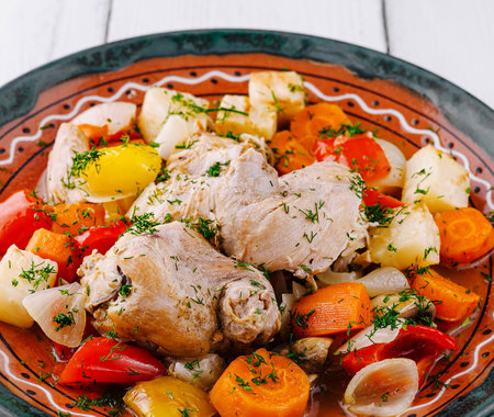 Chicken stew with potatoes, onions, carrots, bell peppers and dill garnish served on a plateの写真素材