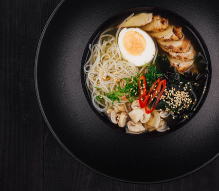 Delicious bowl of chicken ramen is served in a black bowl on a black table setting