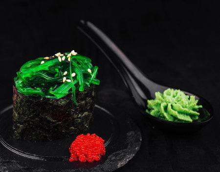 Sushi piece with chuka seaweed, sesame seeds and wasabi paste on black backgroundの写真素材