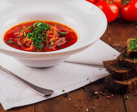 White bowl is brimming with delicious red borscht, garnished with fresh herbs and served alongside rye breadの写真素材
