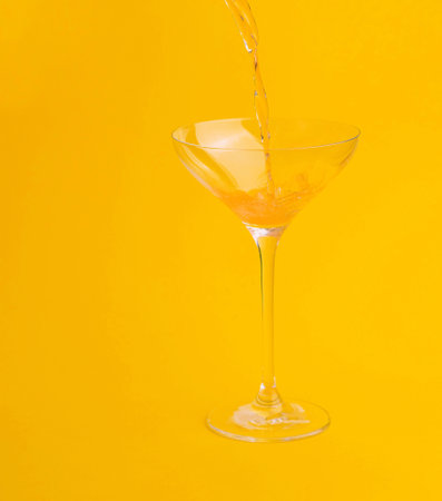 Refreshing drink is being prepared by pouring orange juice into a glass on a vibrant yellow backgroundの写真素材