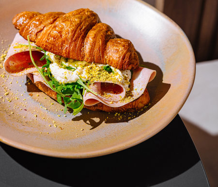 Croissant sandwich with ham, ricotta cheese, arugula and pistachios on plate, close upの写真素材