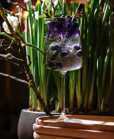 Refreshing cocktail with blueberries and mint, garnished with an edible flower, served on a wooden trayの写真素材