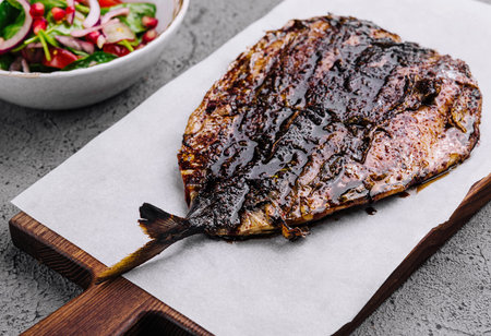 Delicious grilled fish on a wooden board and a bowl of fresh salad, perfect for a healthy meal