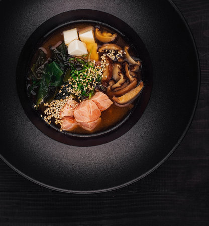 Delicious bowl of miso soup is served in a black bowl placed on a dark wooden tableの写真素材