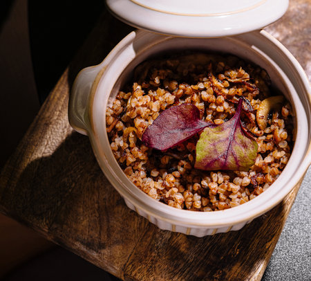 Buckwheat porridge with mushrooms and beetroot leaves served in a ceramic pot on a wooden board, creating a rustic and appetizing culinary sceneの写真素材