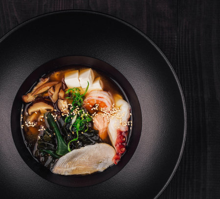 Aromatic soup with tofu, wakame seaweed, shiitake mushrooms and seafood served in black bowlの写真素材