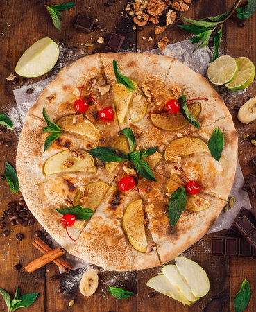 Delicious sweet pizza with apple and cherry lying on a rustic wooden table surrounded by its ingredientsの写真素材