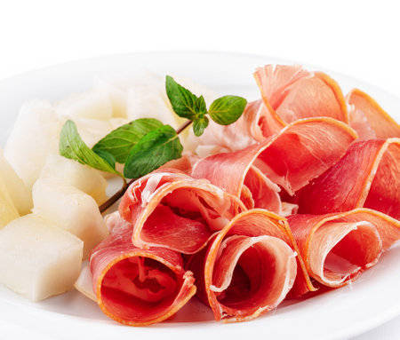 Slices of prosciutto with cantaloupe melon on a white plate garnishing with fresh mintの写真素材