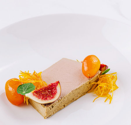 Slice of foie gras is served on a white plate, garnished with figs, kumquat, and edible flowersの写真素材