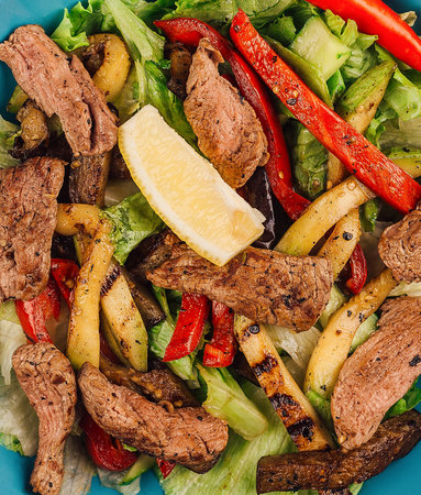 Warm salad with grilled beef slices and roasted vegetables like pepper and zucchini seasoned with lemon juiceの写真素材