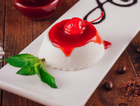 White plate with a dessert that has a cherry on top and a drizzle of chocolate sauceの写真素材