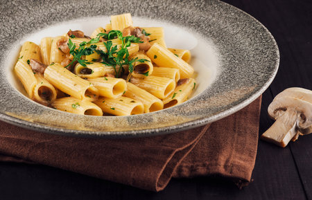 Delicious pasta dish with mushrooms and parsley is served in a modern gray plate on a wooden tableの写真素材