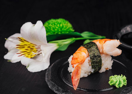 King prawn nigiri sushi served on a black slate plate with soy sauce, wasabi and flowersの写真素材